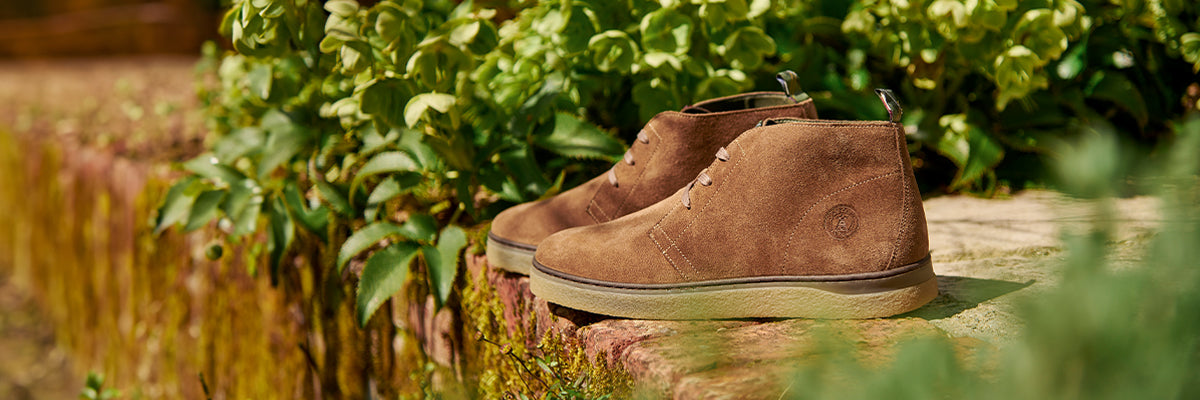 Barbour shoes for men and women displayed outside in a natural setting among greenery.