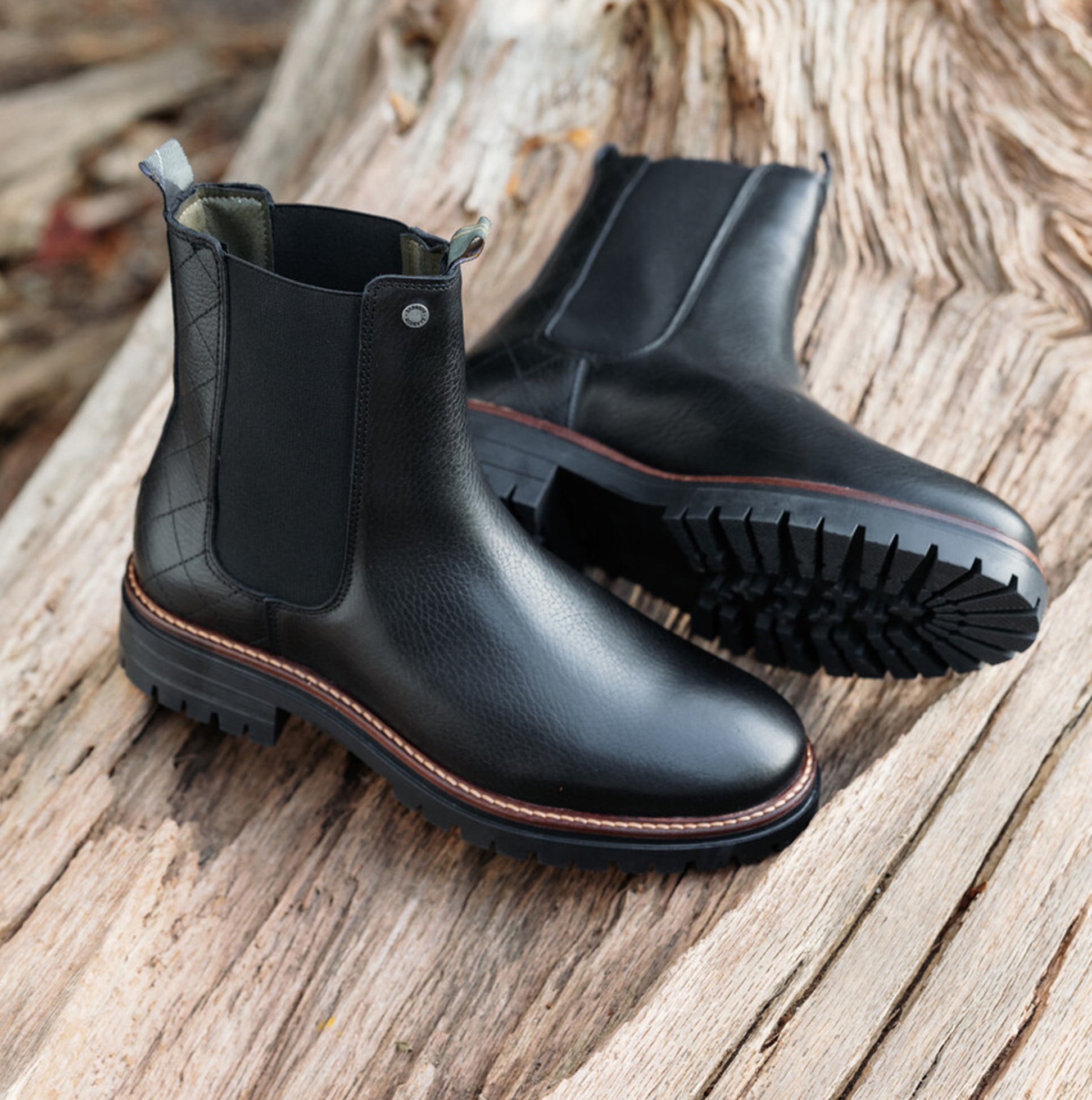 Barbour EVIE Womens Boots Black side view showcasing ankle boots with leather and nylon upper on rustic surface.