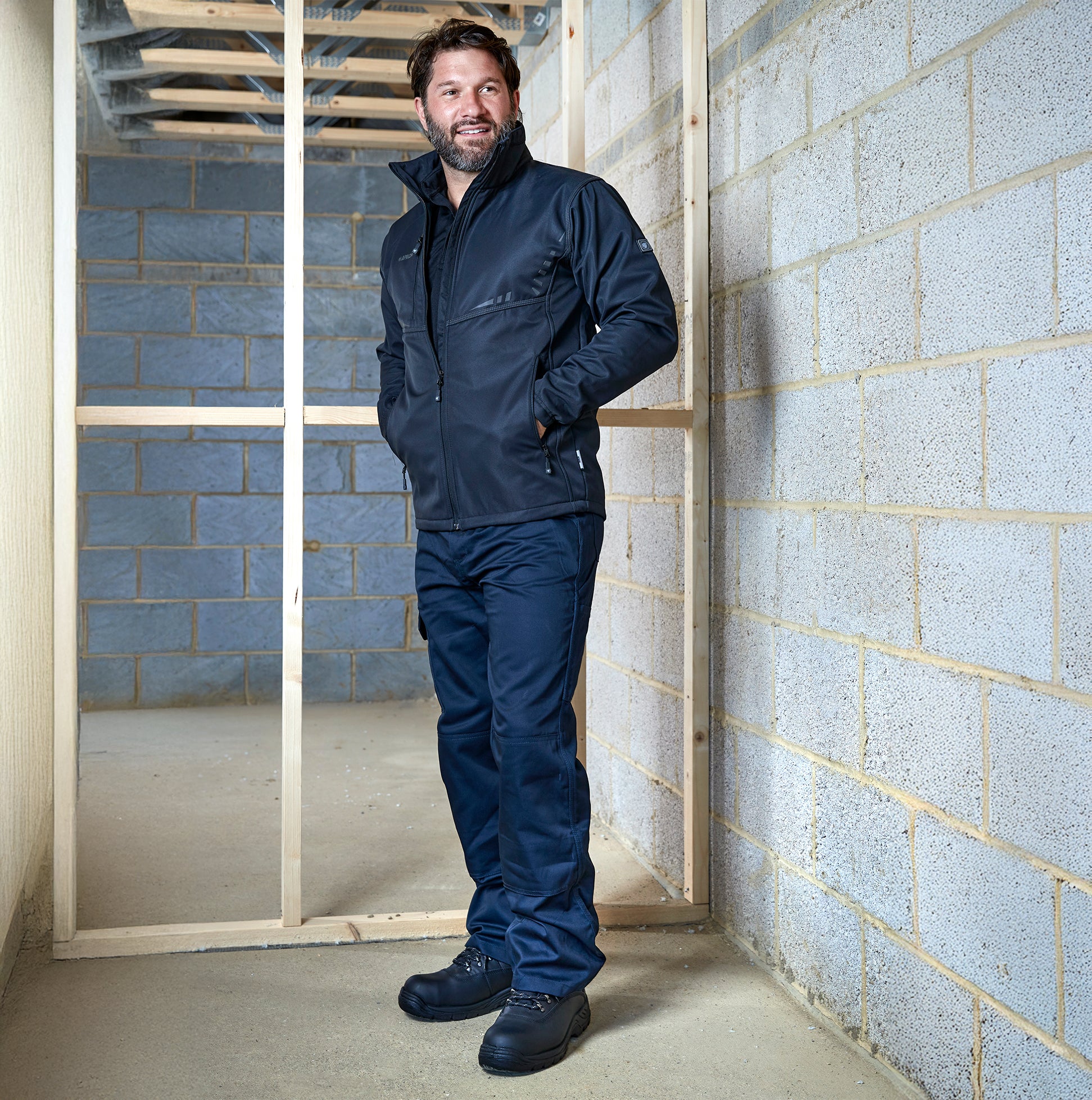 Apache APIND Mens Trousers Navy worn in side view with a matching jacket against a construction background.