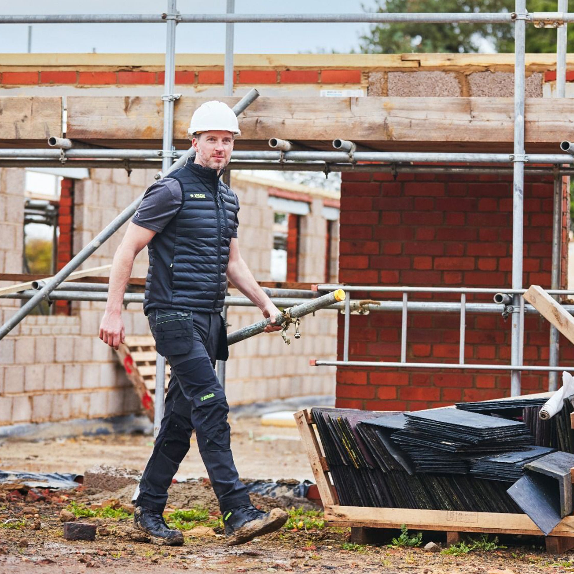 Apache CALGARY Mens Trousers Grey Black front view worn by a worker on a construction site with scaffolding.