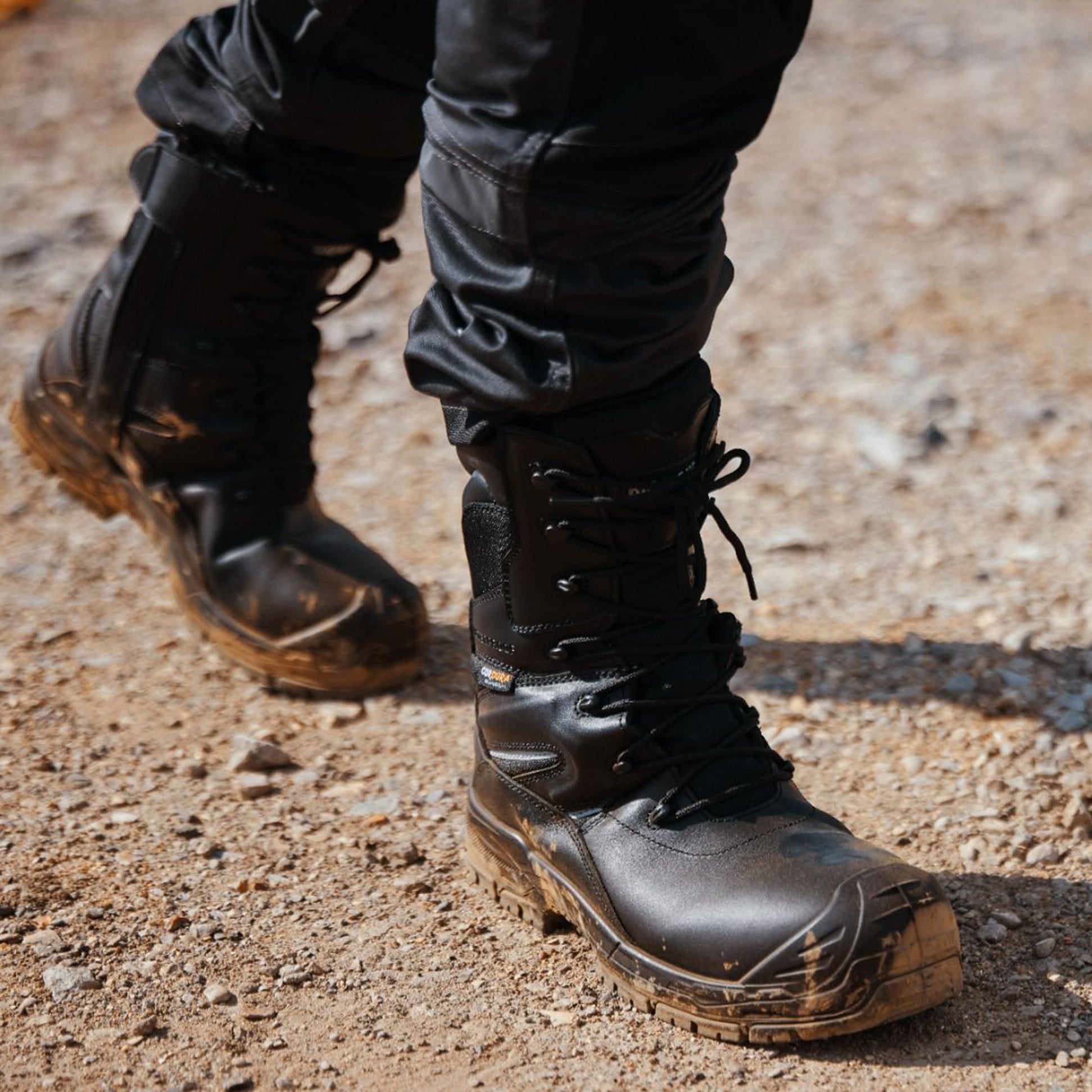 Apache COMBAT Unisex Boots Black side view showing lace-up closure and durable rubber sole on rocky terrain.