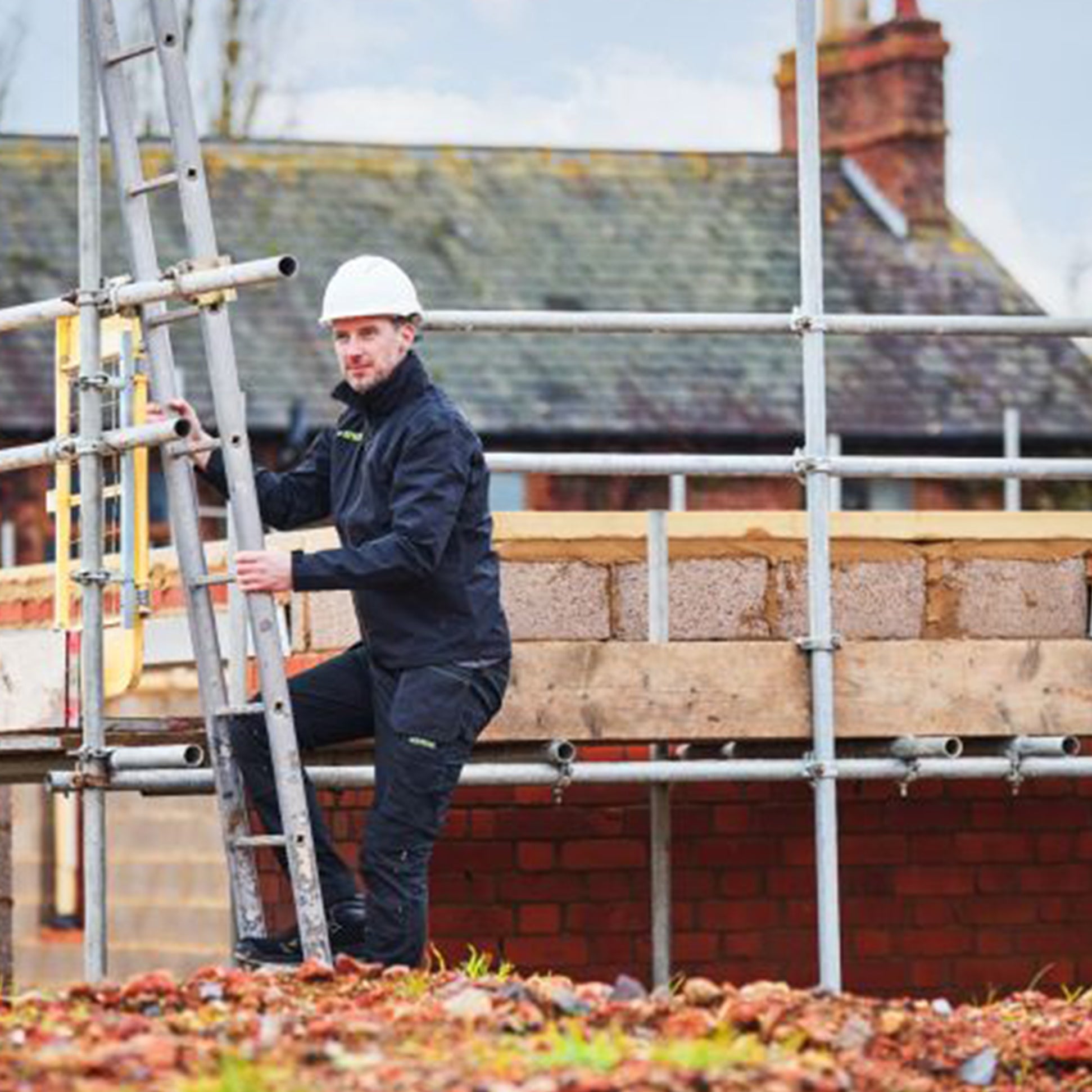 Apache SUDBURY Mens Trousers Black worn by man on scaffolding, climbing ladder, front view, showcasing workwear style.