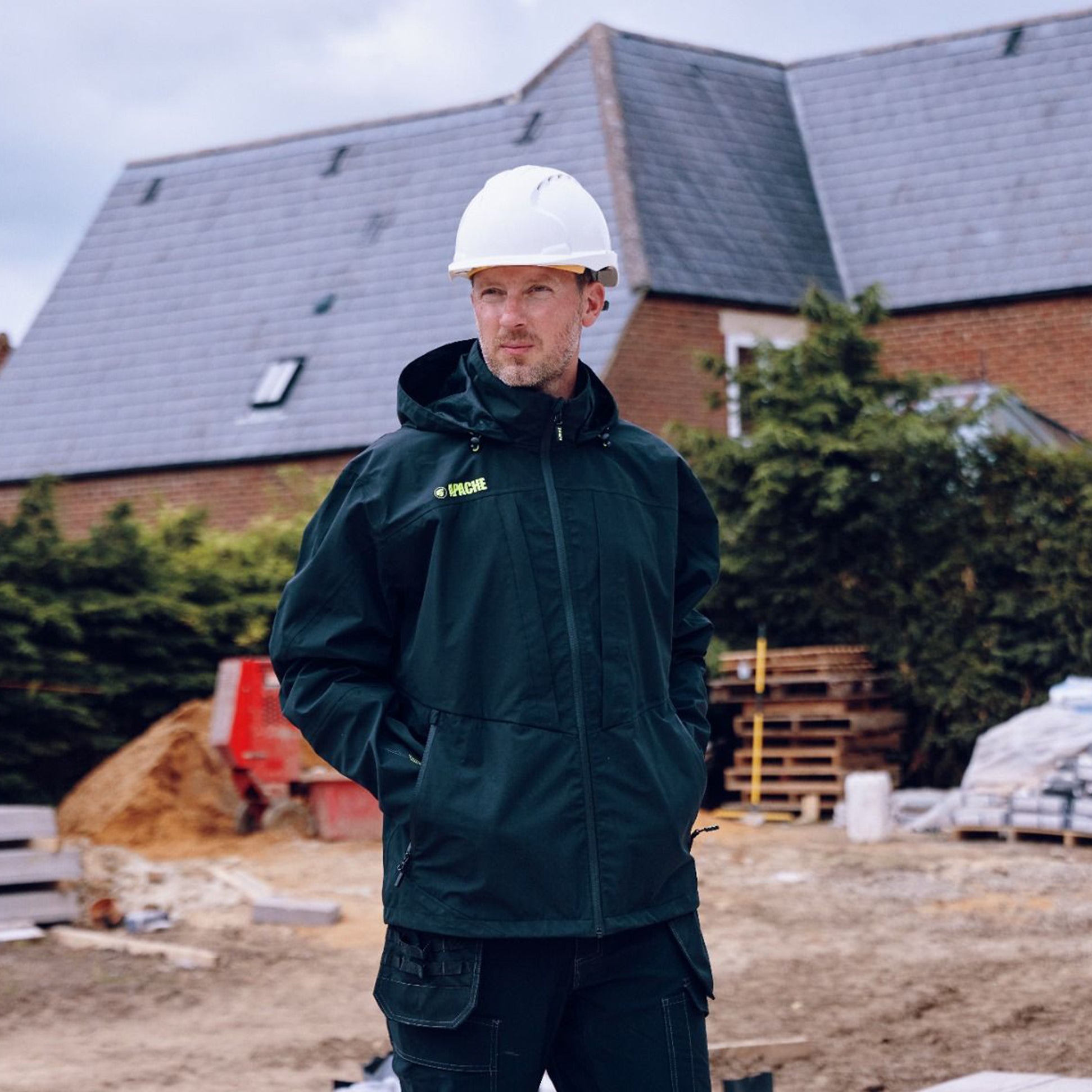 Apache WELLAND Mens Work Jacket Black Charcoal front view on model at construction site, wearing hard hat.