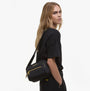 Barbour B.INTL QUALIFY Womens Crossbody Bag Black side view on model, showcasing adjustable strap and zipped pockets.
