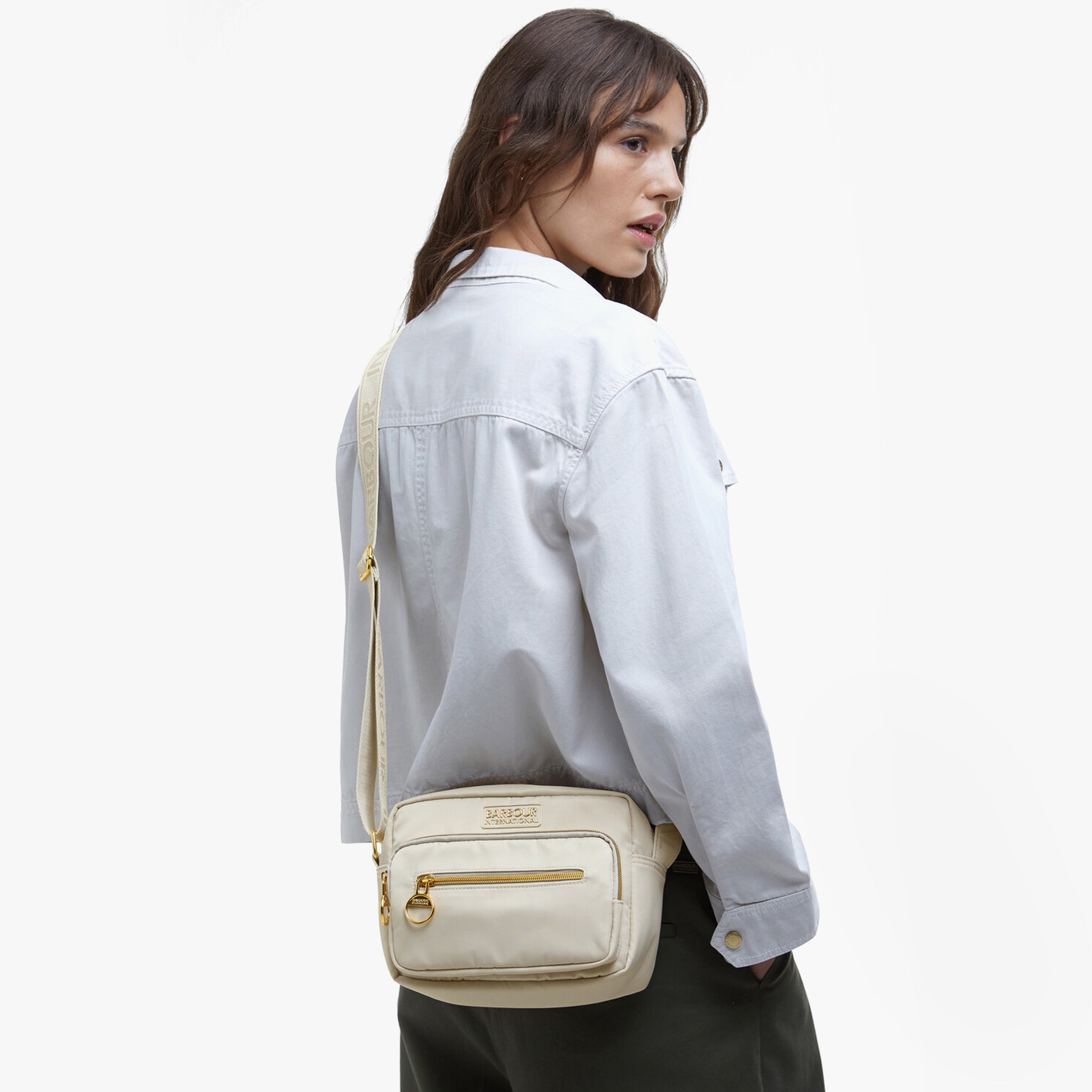Barbour B.INTL QUALIFY Womens Crossbody Bag Light Pearl side view on model, showcasing adjustable strap and zipped pockets.