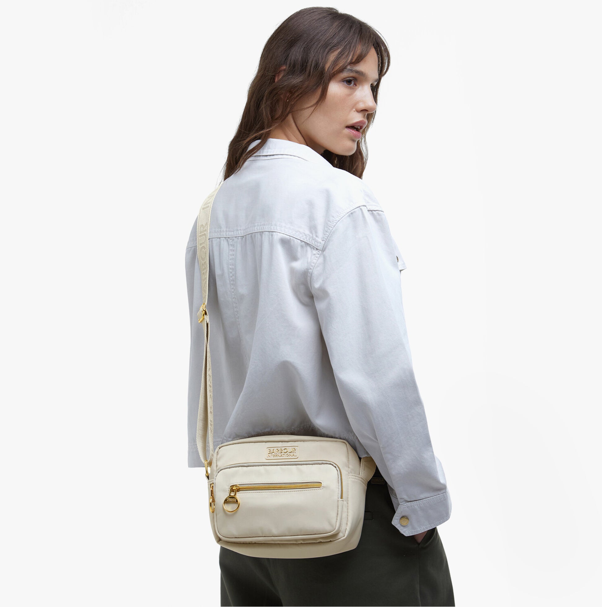 Barbour B.INTL QUALIFY Womens Crossbody Bag Light Pearl side view on model, showcasing adjustable strap and zipped pockets.