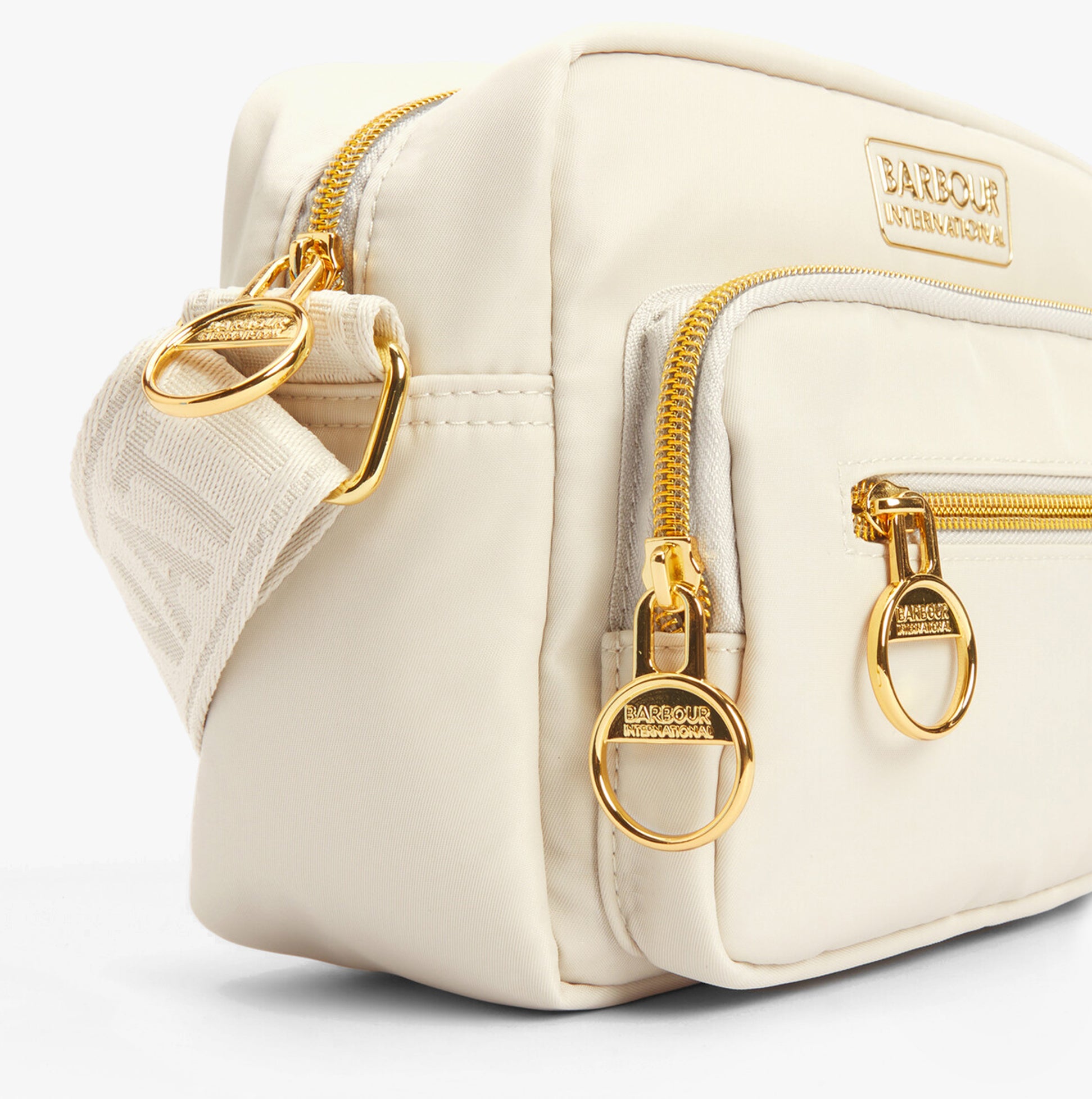 Barbour B.INTL QUALIFY Womens Crossbody Bag Light Pearl side view showcasing zip closures and gold hardware.