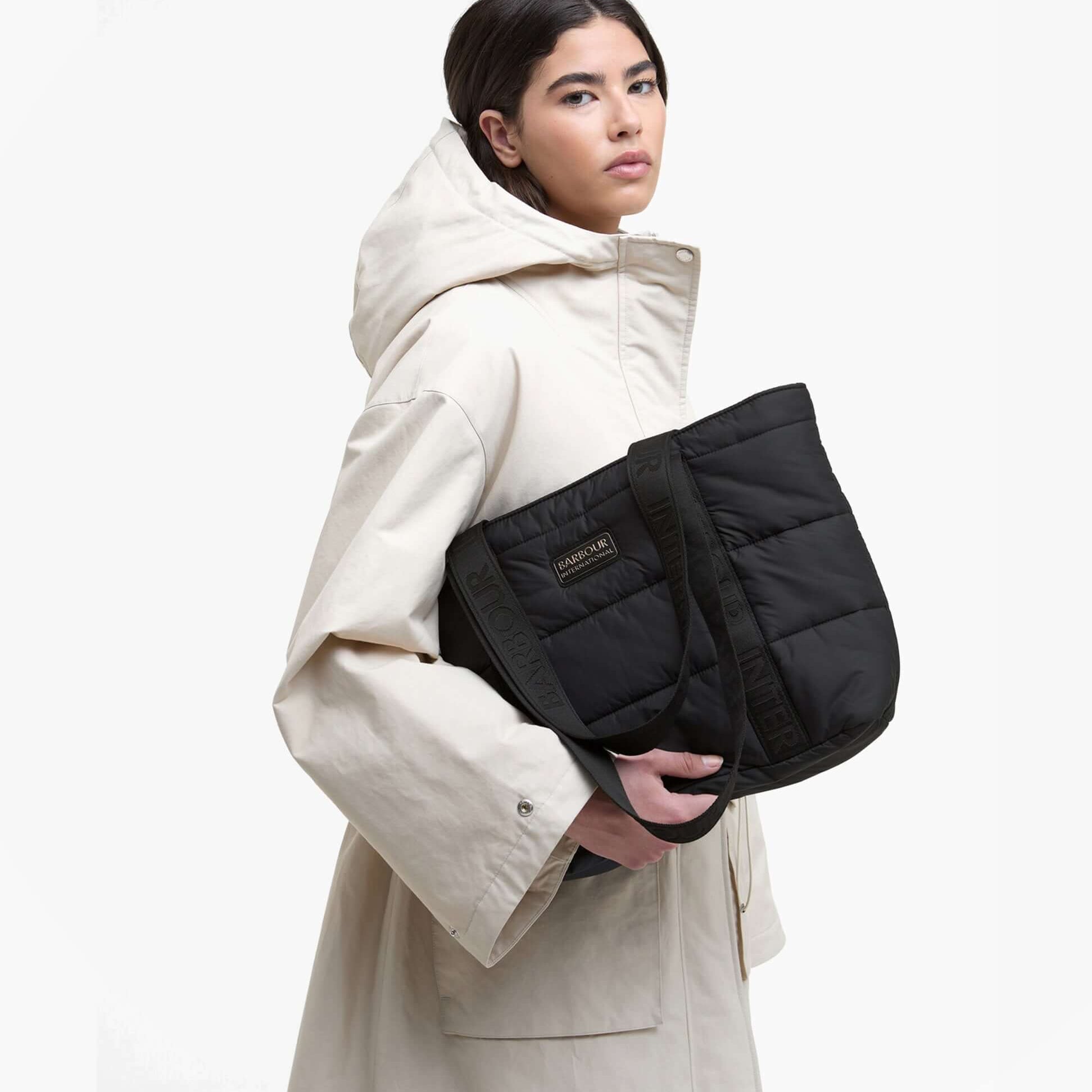 Barbour MONACO QUILT Tote Bag Womens Black front view, held by model in cream coat, showcasing zip closure and quilted design.