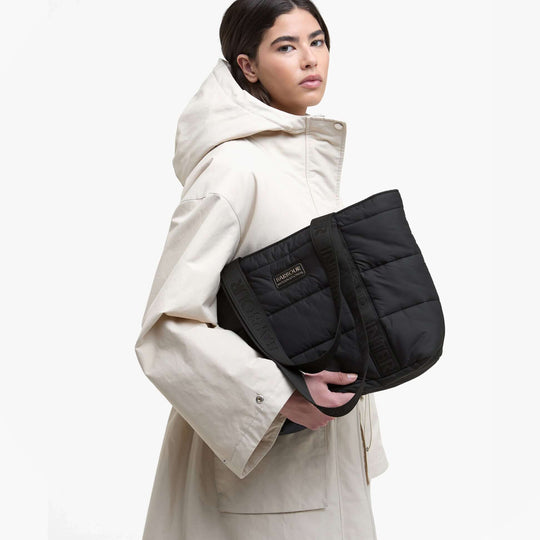 Barbour MONACO QUILT Tote Bag Womens Black front view, held by model in cream coat, showcasing zip closure and quilted design.