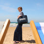 Barbour LOGO Womens Holiday Tote Bag Navy/Stone side view on the beach with a model, wearing striped top and jeans.