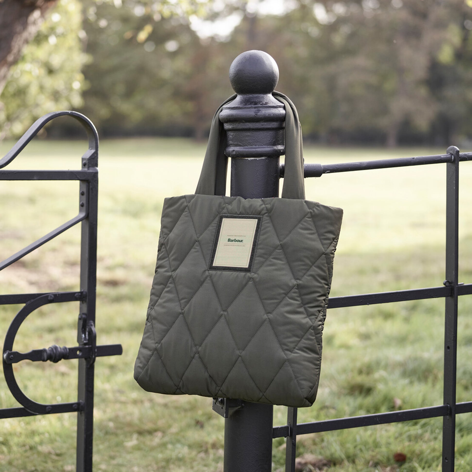 Barbour MARIAH QUILTED Womens Tote Bag Olive hanging on a fence post, showcasing its quilted design and woven logo.