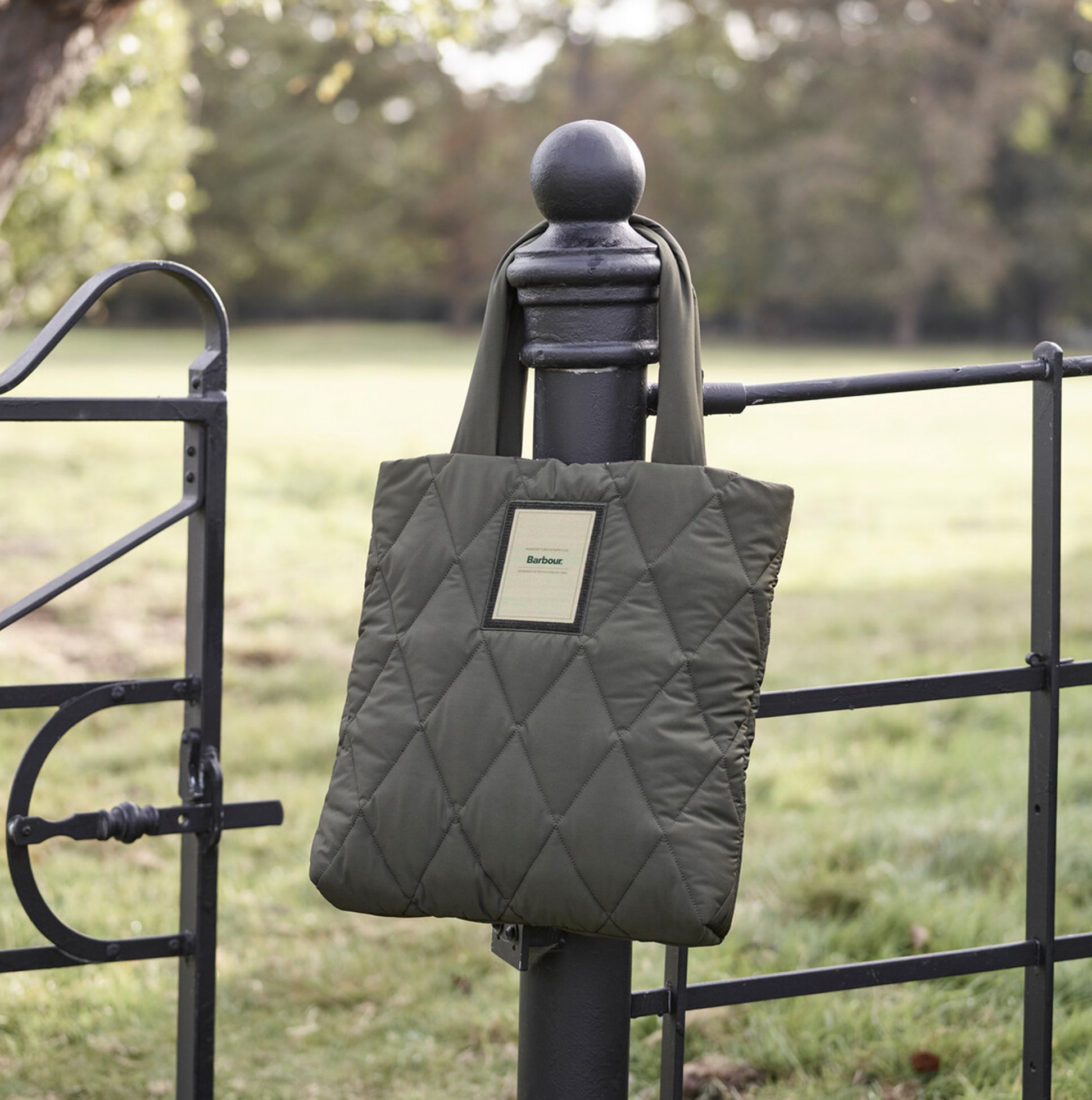 Barbour MARIAH QUILTED Womens Tote Bag Olive hanging on a fence post, showcasing its quilted design and woven logo.