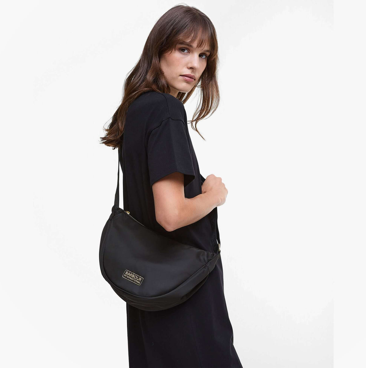 Barbour QUALIFY Womens Sling Bag Black side view worn with black outfit, showcasing stylish design and zip closure.