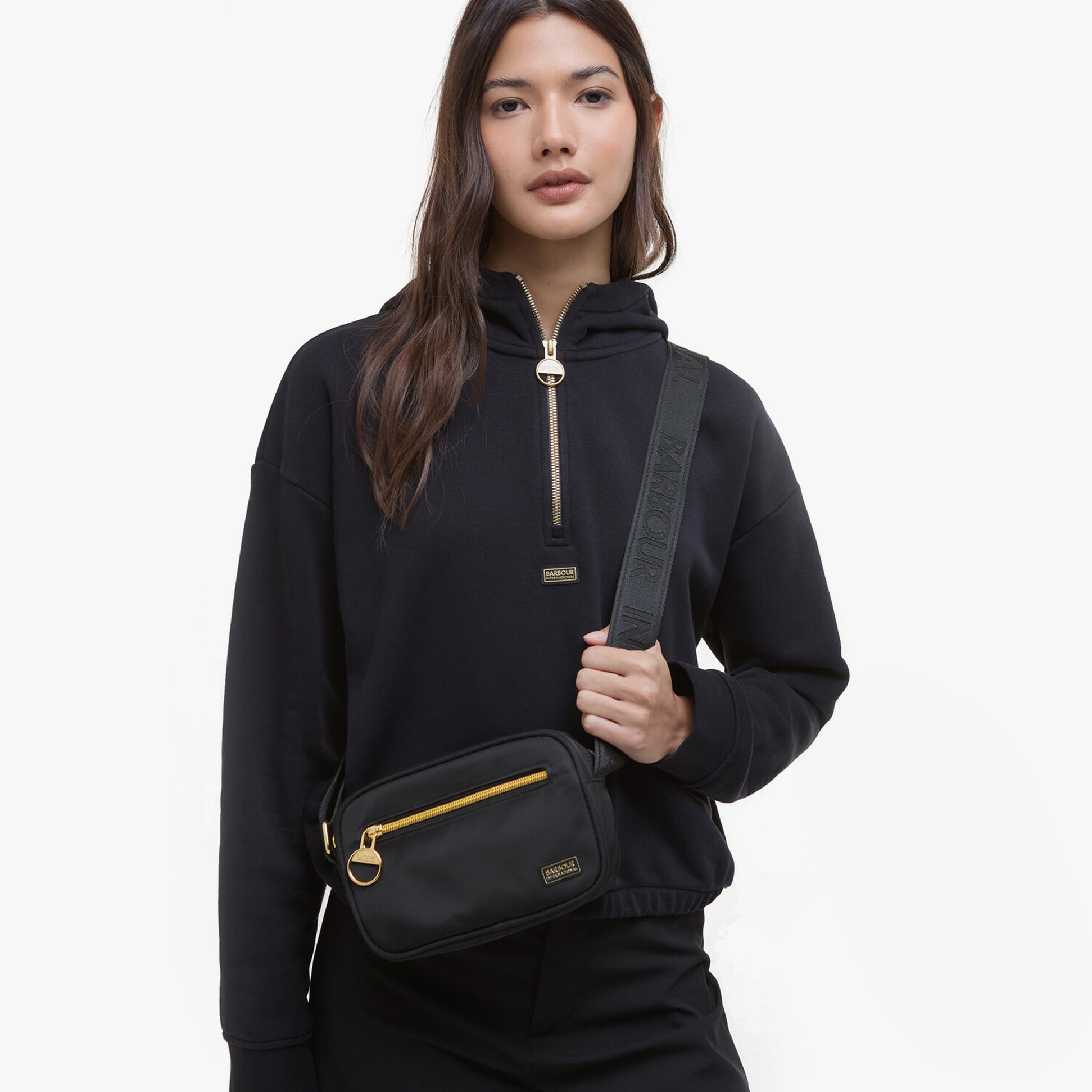 Barbour B.INTL MICRO QUALIFY Womens Crossbody Bag Black worn by model in front view, featuring adjustable strap and zip closure.