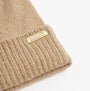 Barbour SPARKLE BEANIE & SCARF Womens Gift Set Oat detail view of the beanie with logo tag on a beige background.