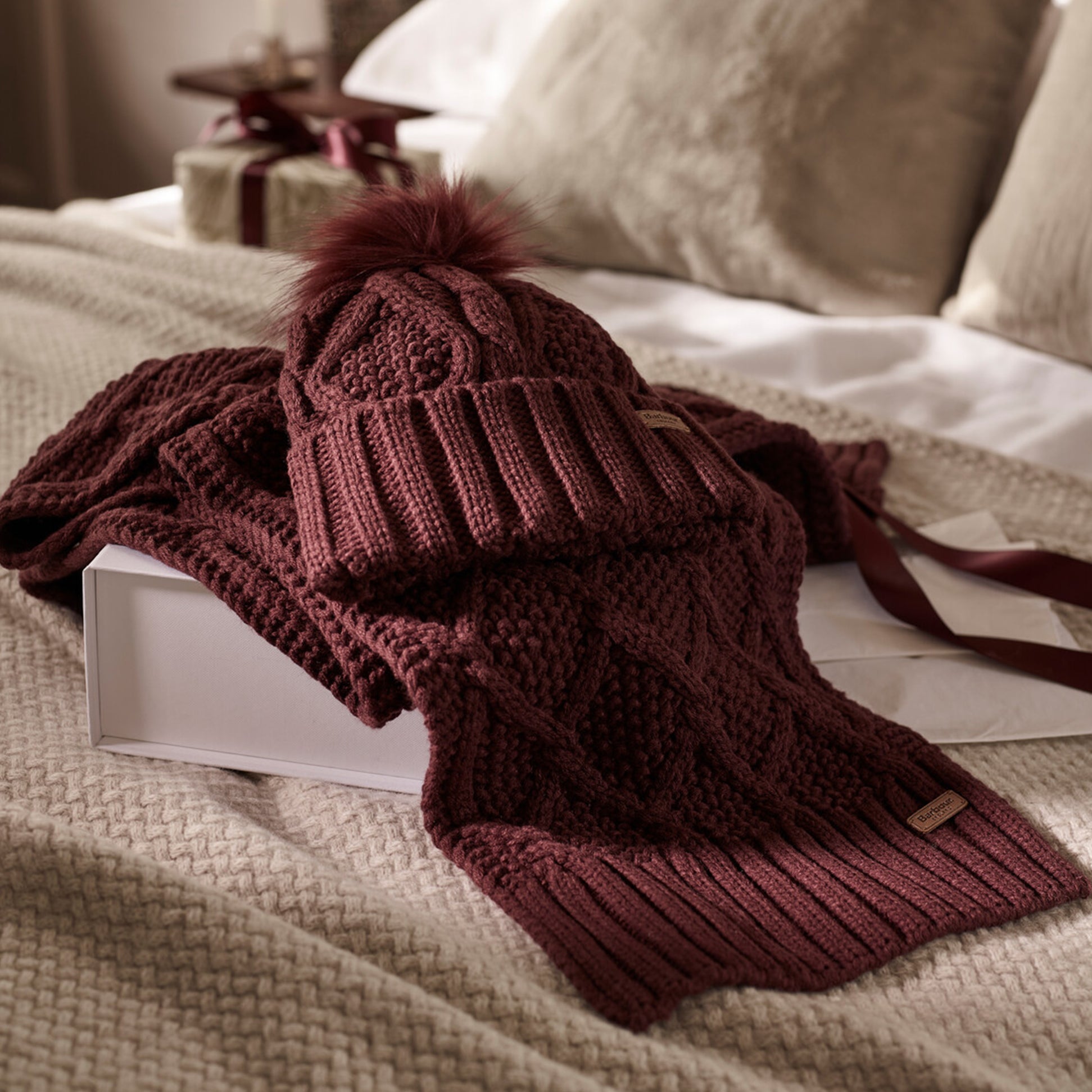 Barbour RIDLEY BEANIE & SCARF Gift Set Womens Cabernet front view showing textured knit beanie and matching scarf on a cozy bed.