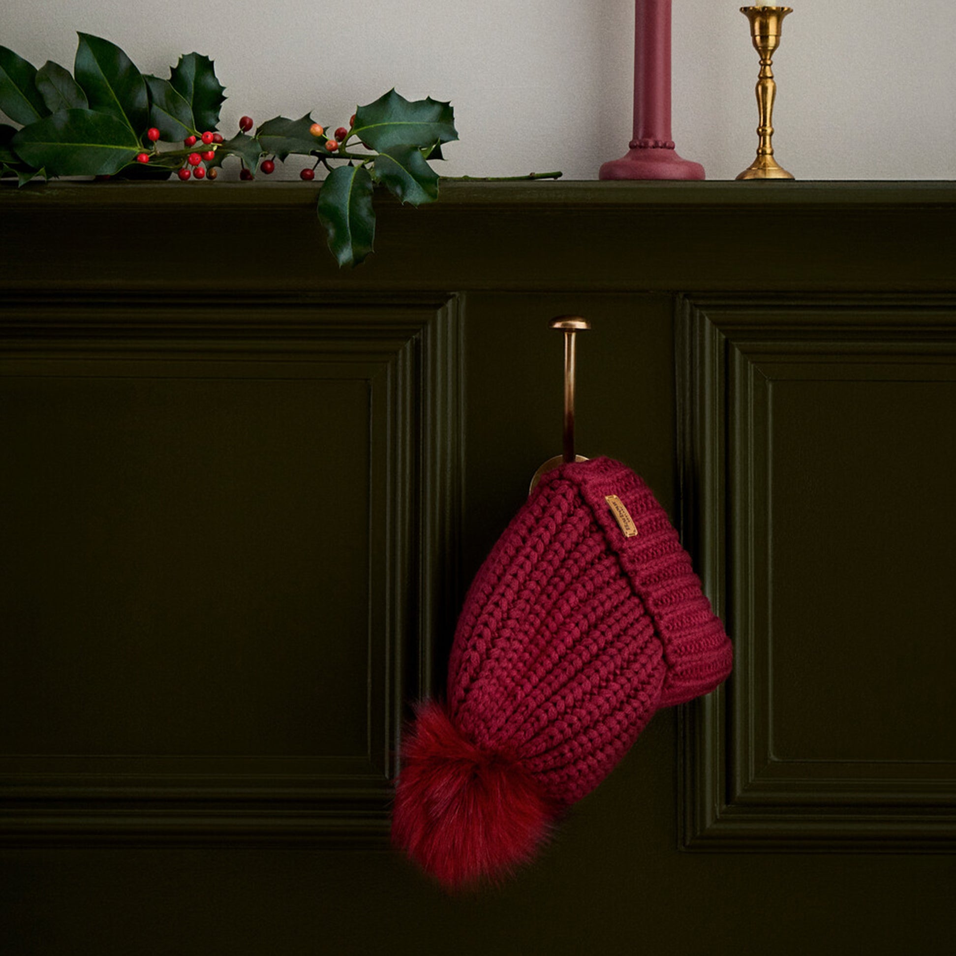 Barbour SALTBURN Womens Beanie Biking Red hanging on a hook with faux fur pom, stylish knit design.