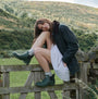 Barbour WILTON Womens Chelsea Wellington Boots Olive side view on model sitting on a fence in a green landscape.