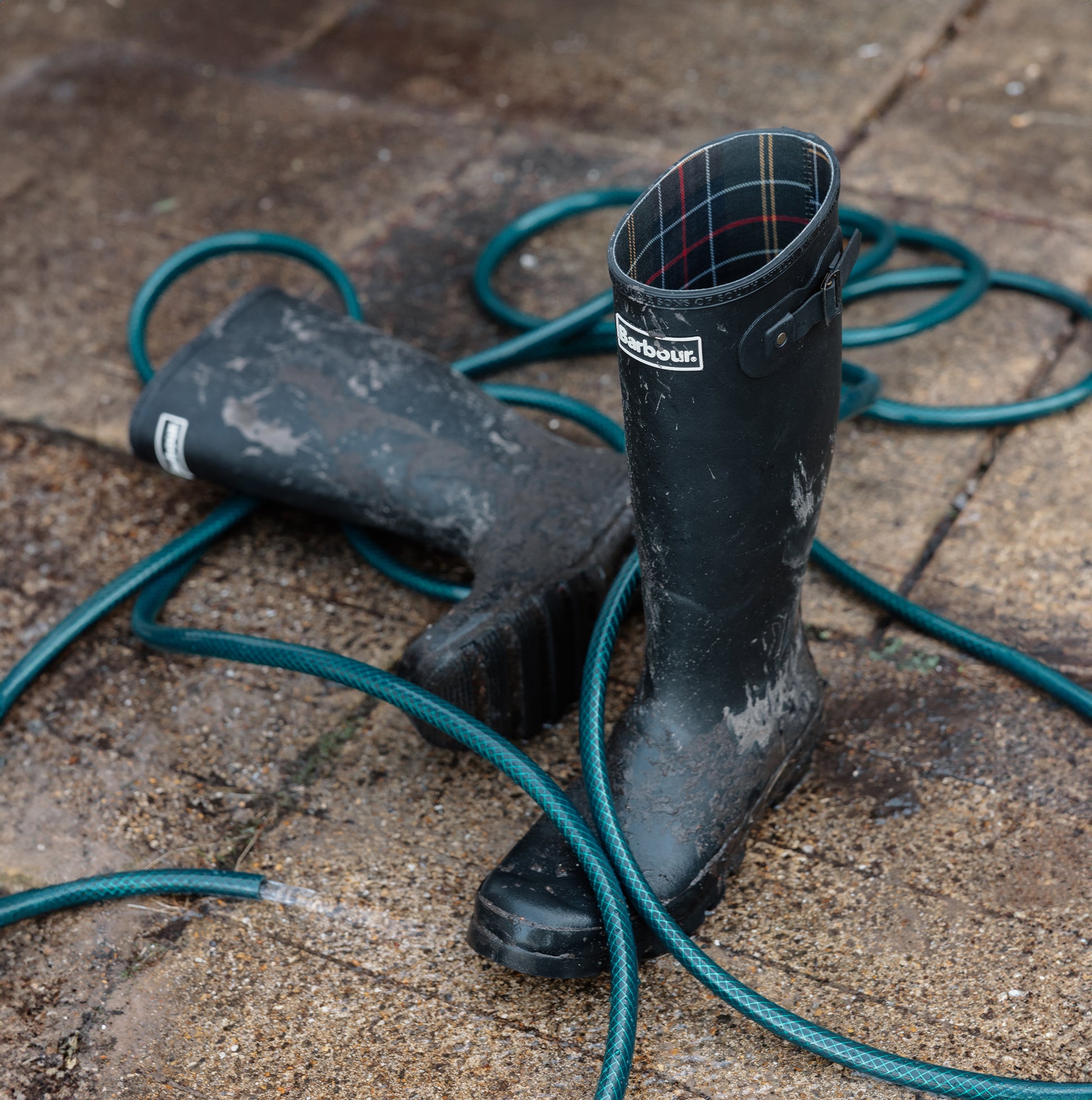 Barbour SNOWDON Womens Tall Wellies Black side view on muddy ground with garden hose.