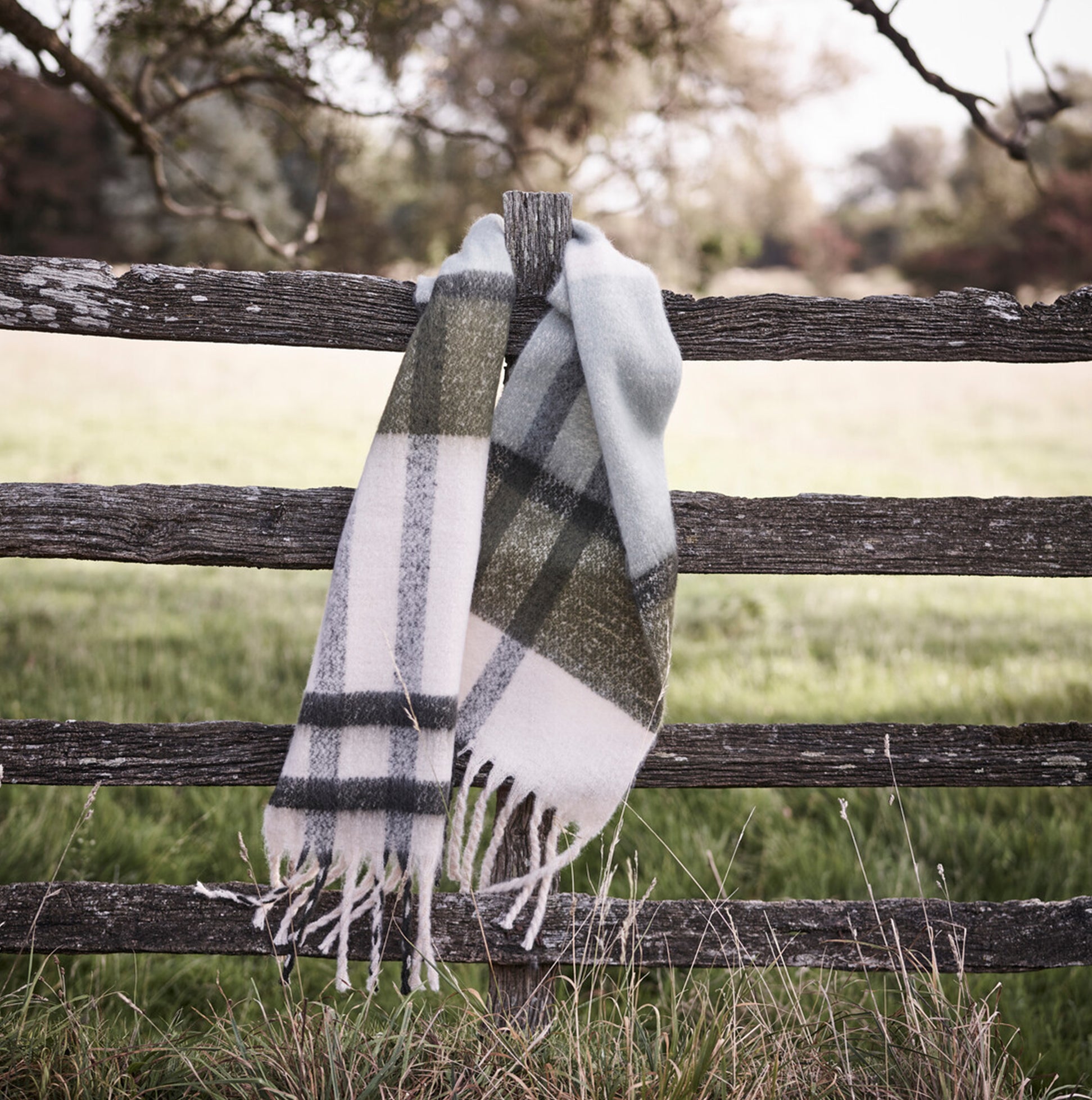 Barbour ISLA TARTAN BOUCLE Scarf Womens Soft Mint hanging on a wooden fence, showcasing the tartan pattern and tasselled trims.