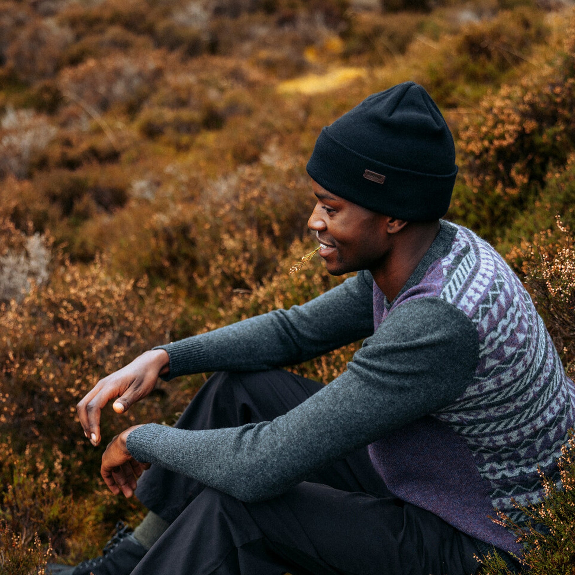 Barbour HEALEY Mens Beanie Black worn by man sitting outdoors, side view, surrounded by nature.