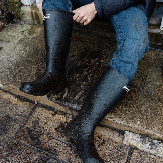 Barbour BEDE Mens Tall Wellington Boots Black side view worn outdoors, showcasing waterproof design and knee-high shaft.