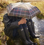 Barbour TARTAN FULL LENGTH Classic Umbrella shown in use under a rainy setting near a stream, providing stylish protection.
