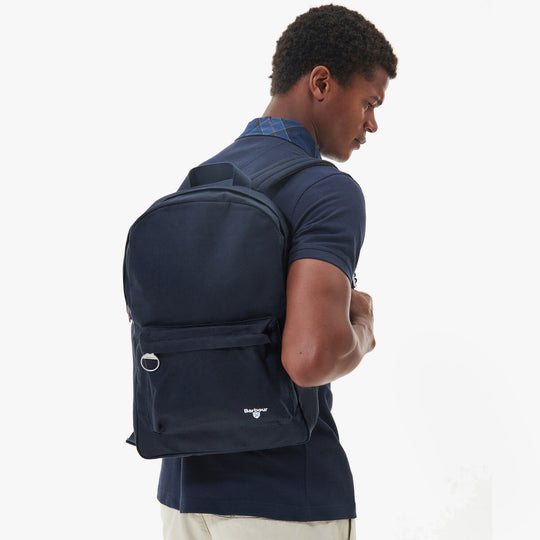 Barbour CASCADE Unisex Adults Backpack Navy side view worn by a model showcasing adjustable shoulder straps.