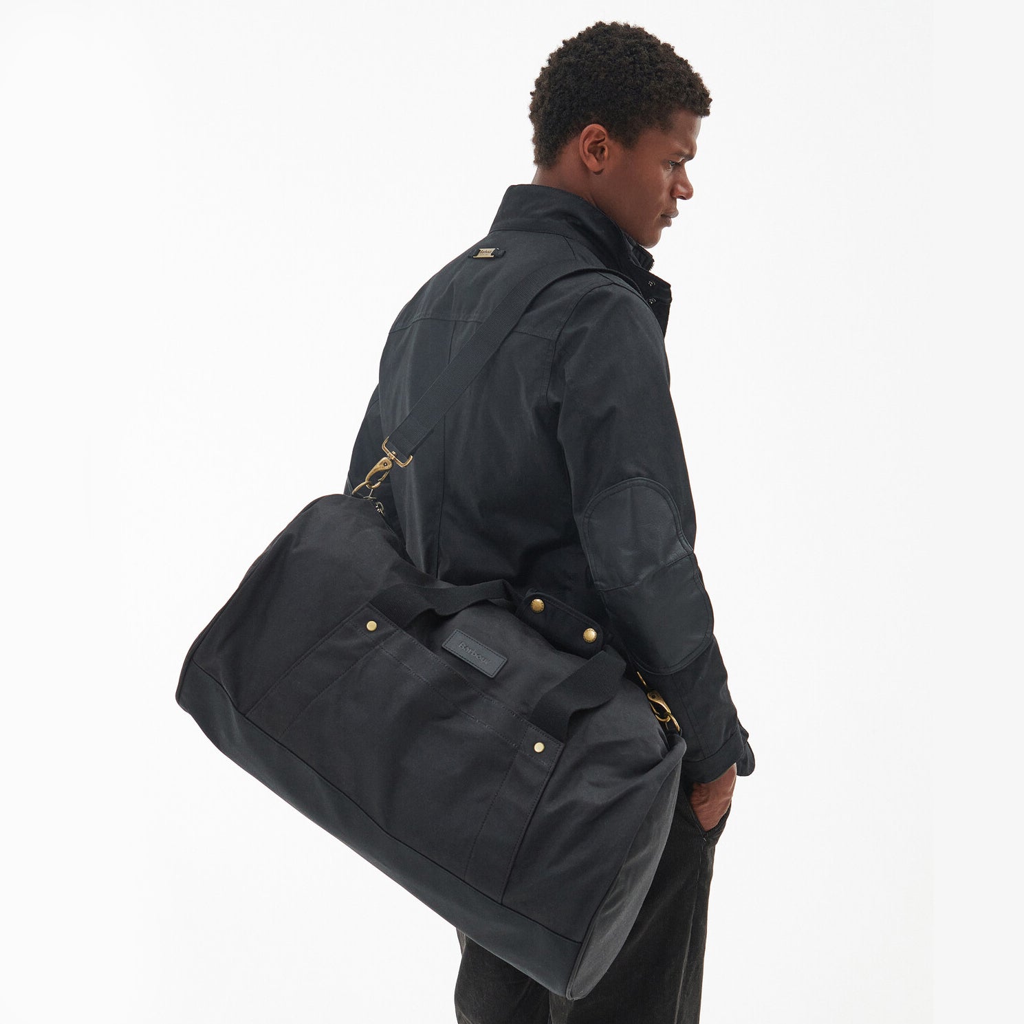 Barbour EXPLORER WAX Unisex Adults Duffle Bag Black side view with model carrying the bag over shoulder.