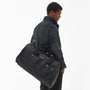 Barbour EXPLORER WAX Unisex Adults Duffle Bag Black side view with model carrying the bag over shoulder.