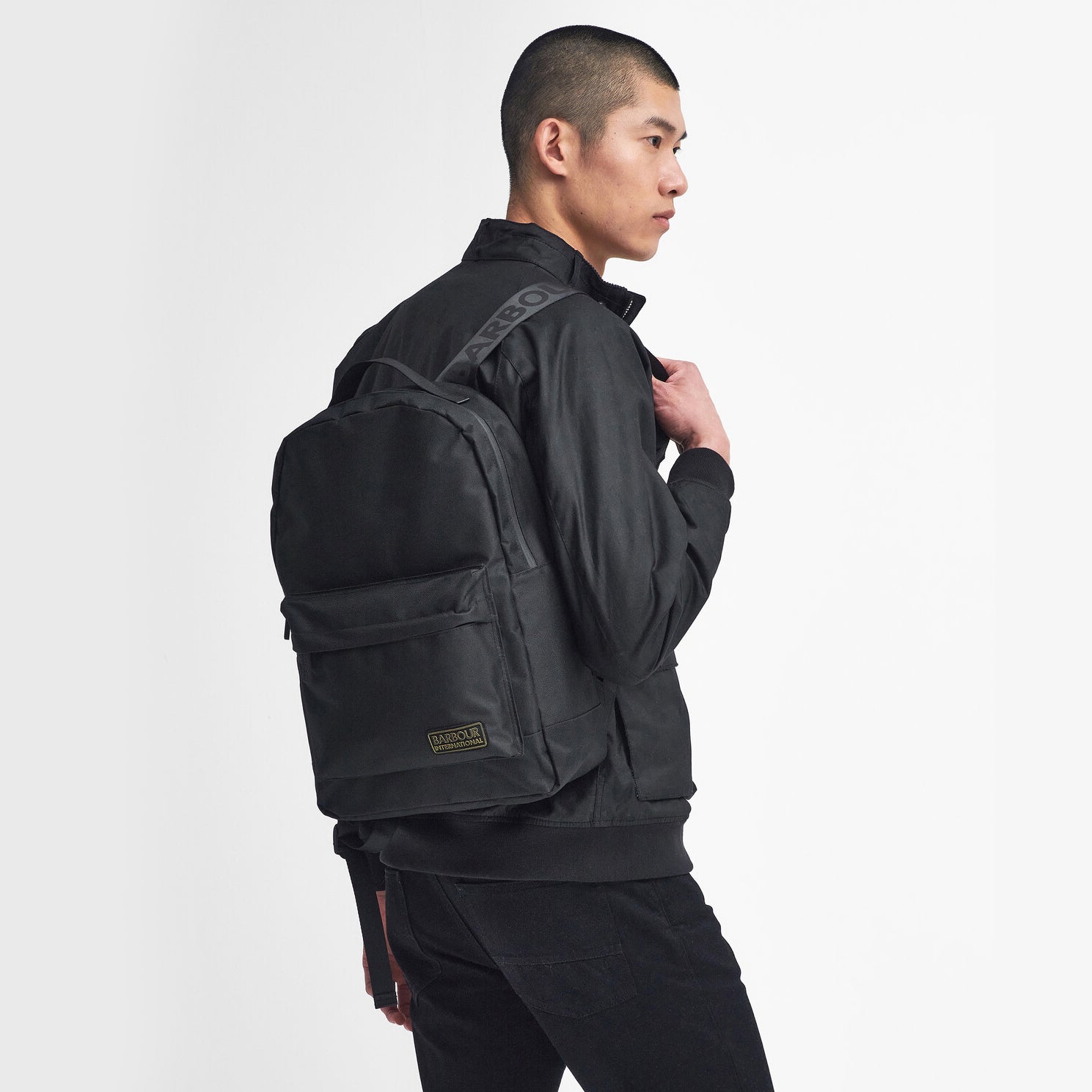 Barbour KNOCKHILL ESSENTIAL BACKPACK Unisex Adults Backpack Black side view on model wearing black jacket.