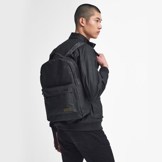 Barbour KNOCKHILL ESSENTIAL BACKPACK Unisex Adults Backpack Black side view on model wearing black jacket.
