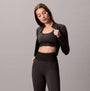Calvin Klein Medium Impact Sports Bra front view worn under a black zip-up jacket.