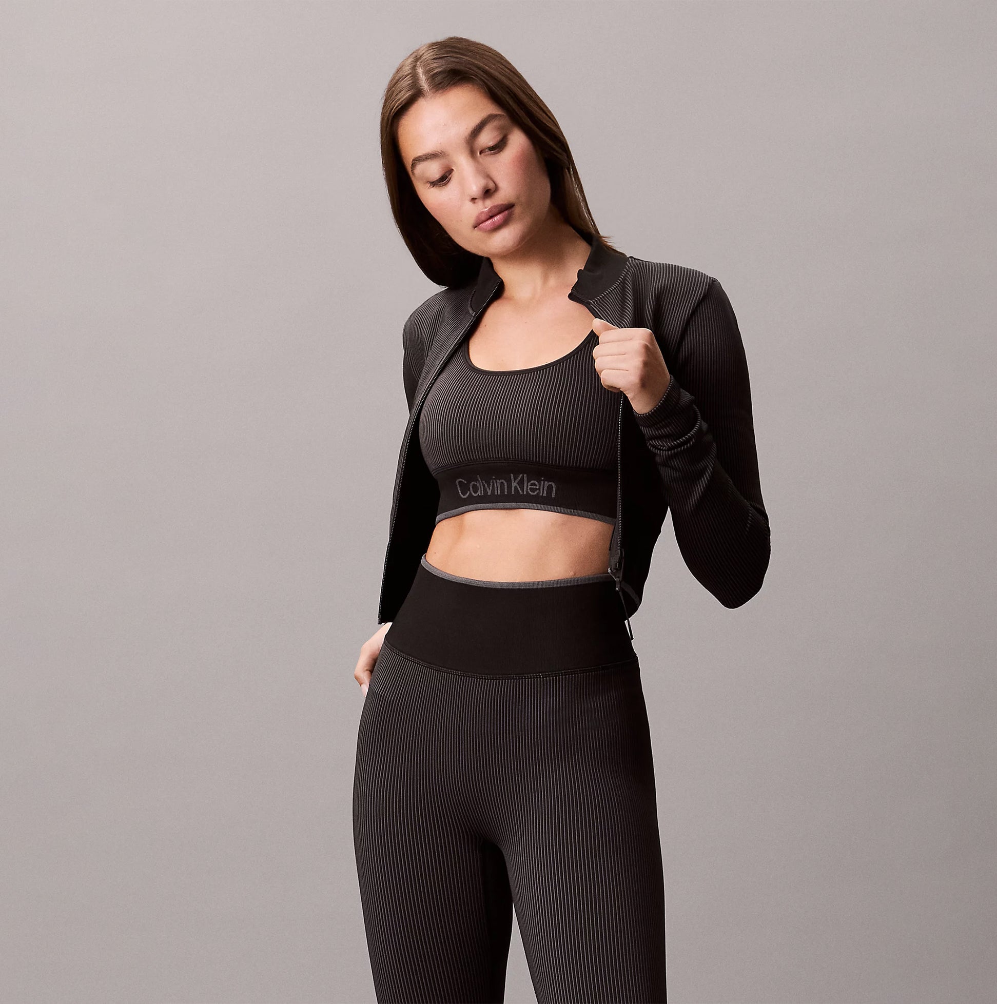 Calvin Klein Medium Impact Sports Bra front view worn under a black zip-up jacket.