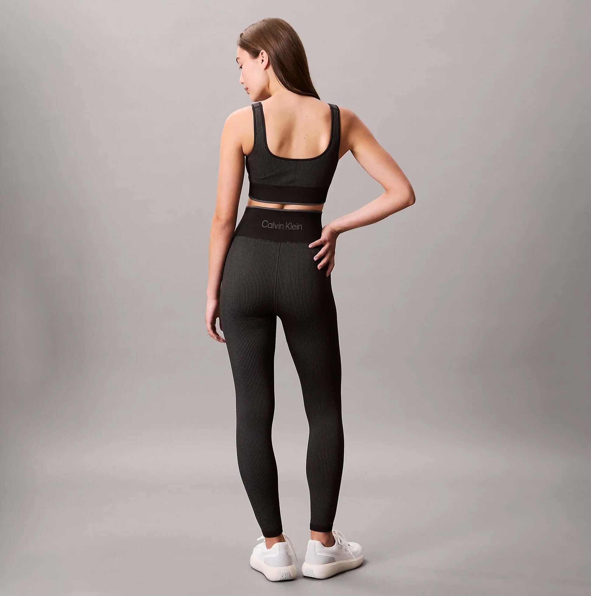 Calvin Klein Medium Impact Womens Sports Bra Black back view model wearing black leggings and athletic shoes.