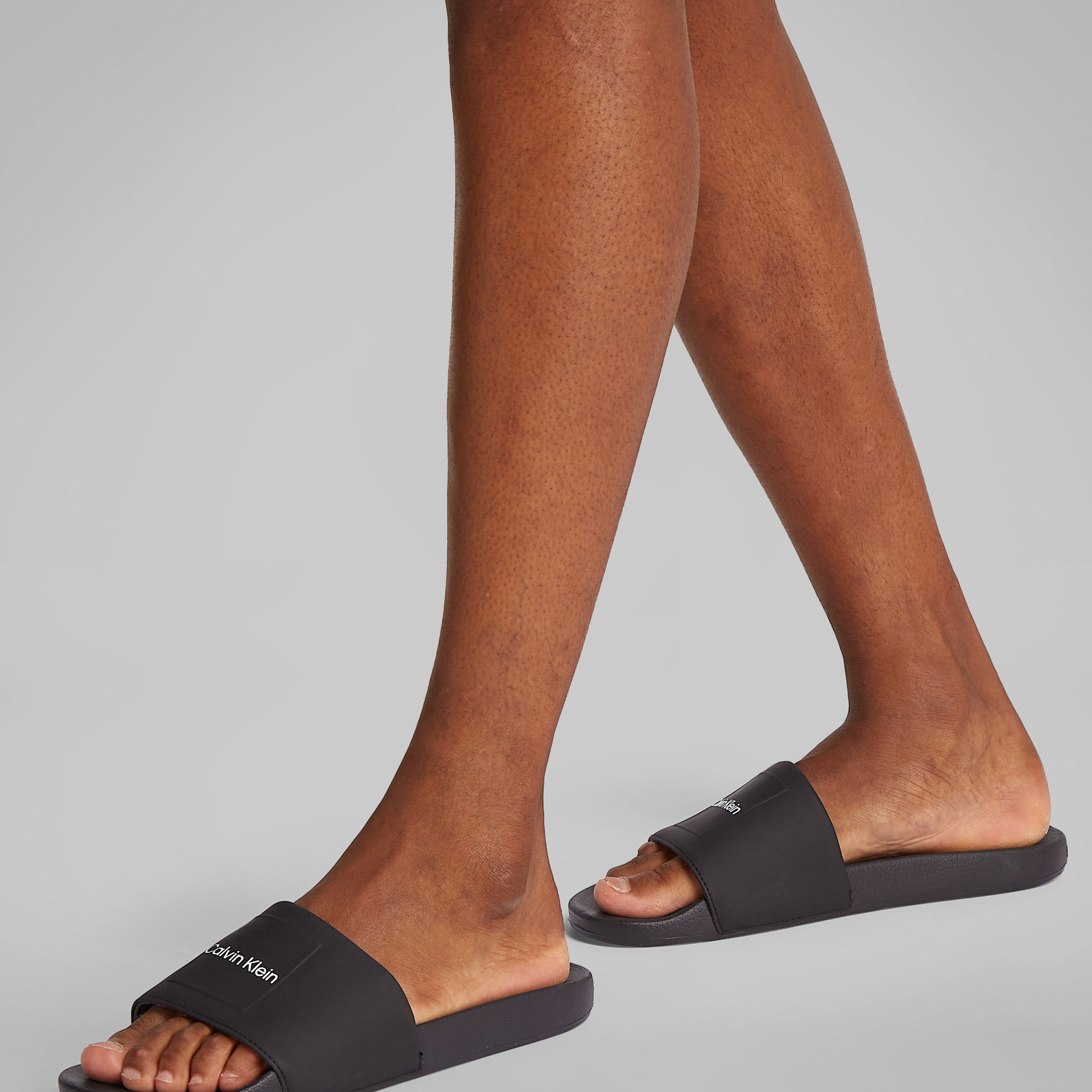 Calvin Klein POOL SLIDE W/ CK SQU Mens Sliders Black side view on model's feet showcasing comfort and style.