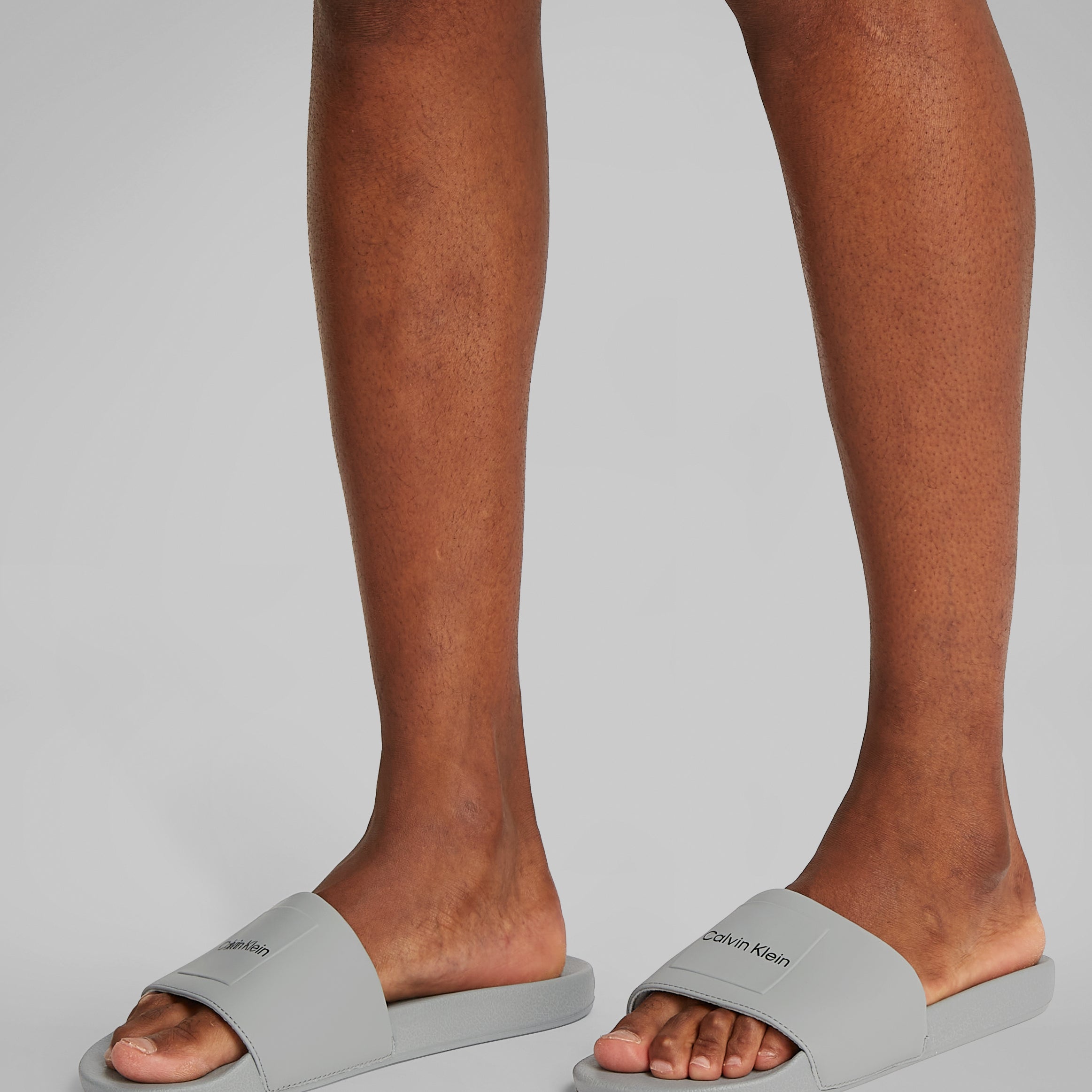 Calvin Klein POOL SLIDE W/ CK SQU Mens Sliders Granite Road side view on model's feet showcasing comfort and lightweight design.