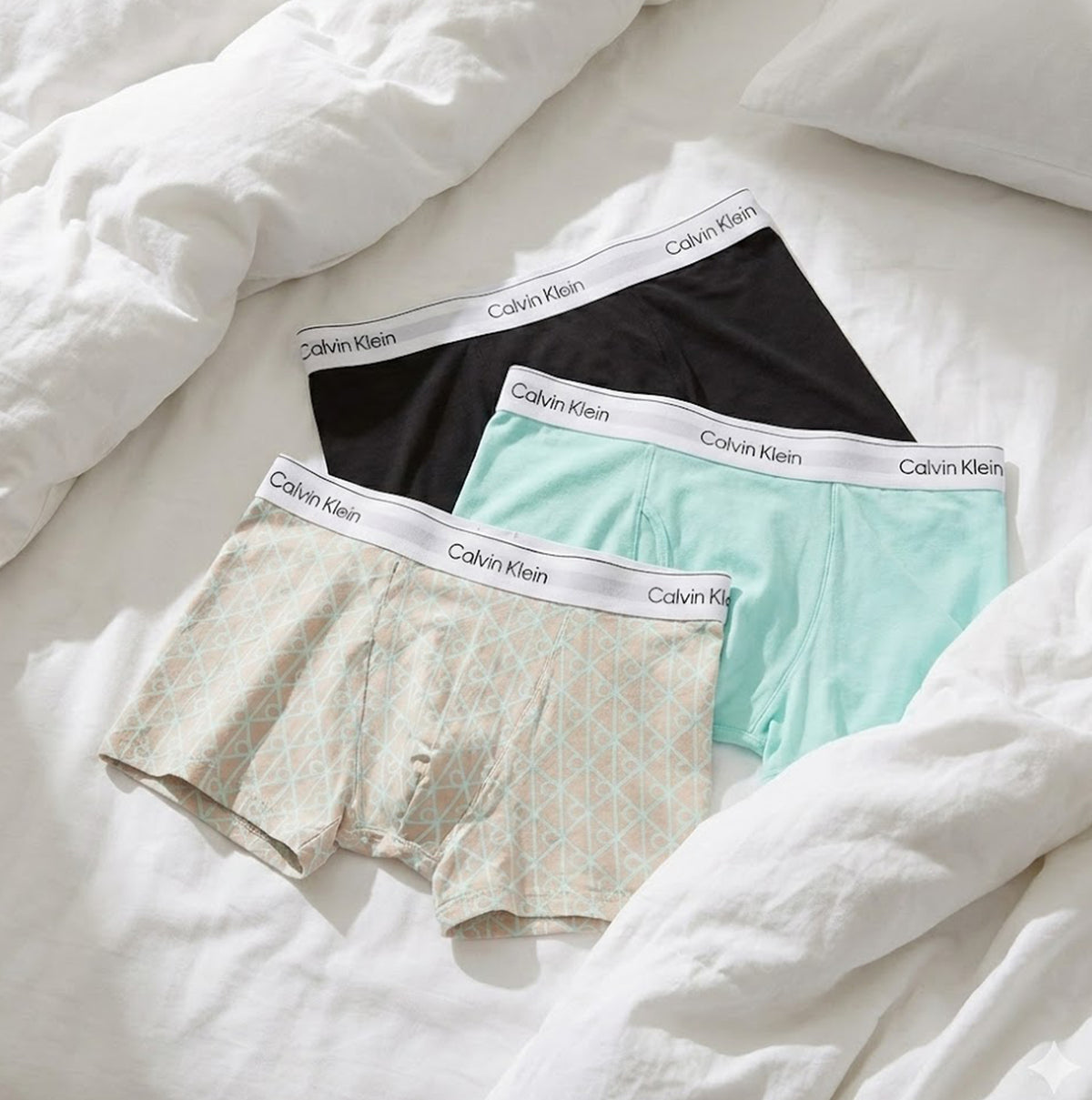 Calvin Klein COTTON BLEND Mens 3 Pack Trunks Multicoloured displayed on a bed, featuring black, mint, and patterned options.