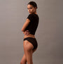 Calvin Klein ICON LOGO Low Rise Womens Bikini Briefs Black side view on model, showcasing semi-sheer finish and logo pattern.