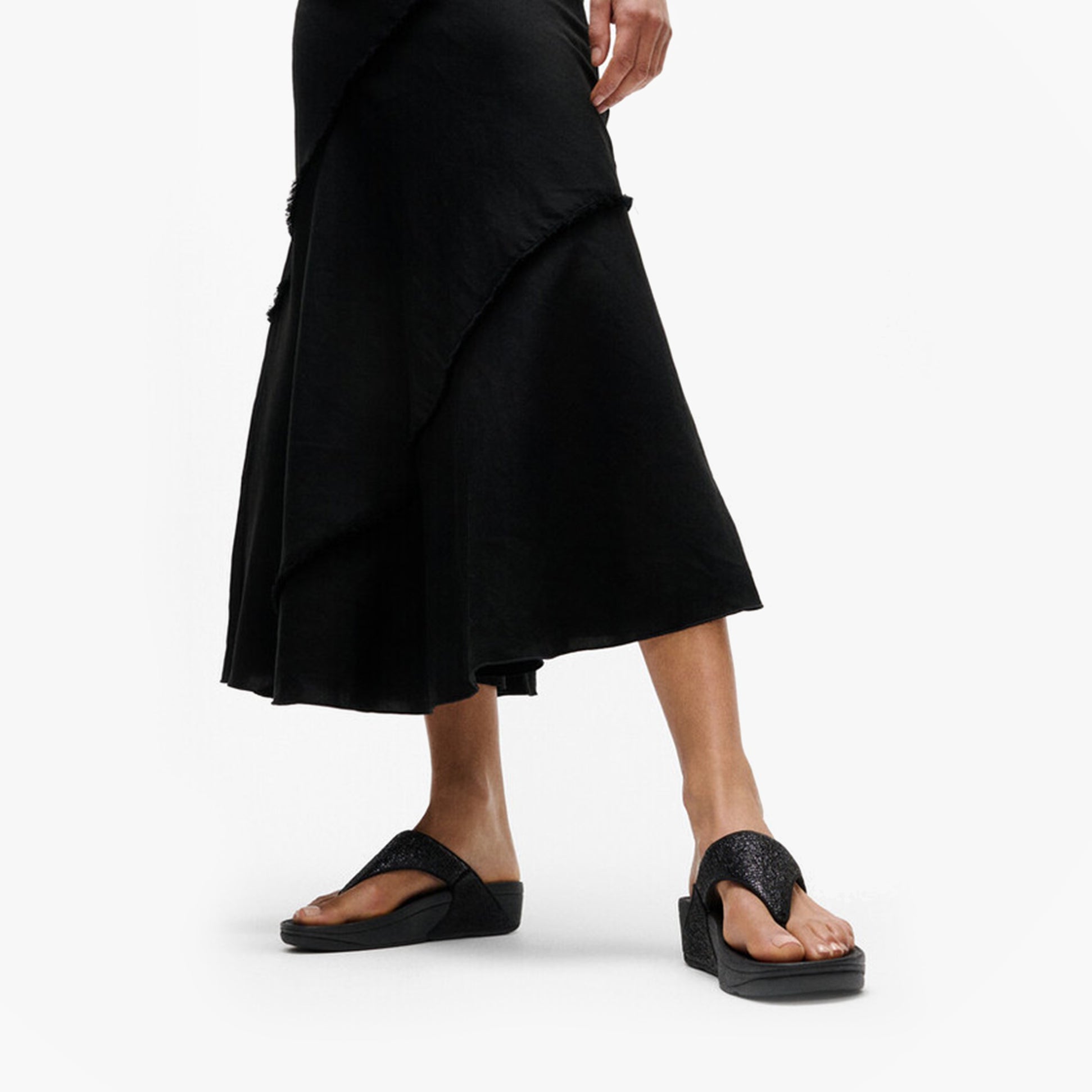 FitFlop LULU CRINKLED-SHIMMER Ladies Toe Post Sandals Metallic Black side view with a model wearing a black skirt.