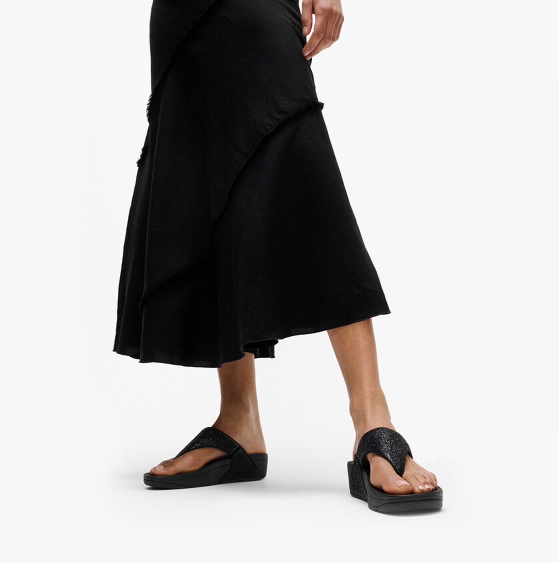 FitFlop LULU CRINKLED-SHIMMER Ladies Toe Post Sandals Metallic Black side view with a model wearing a black skirt.