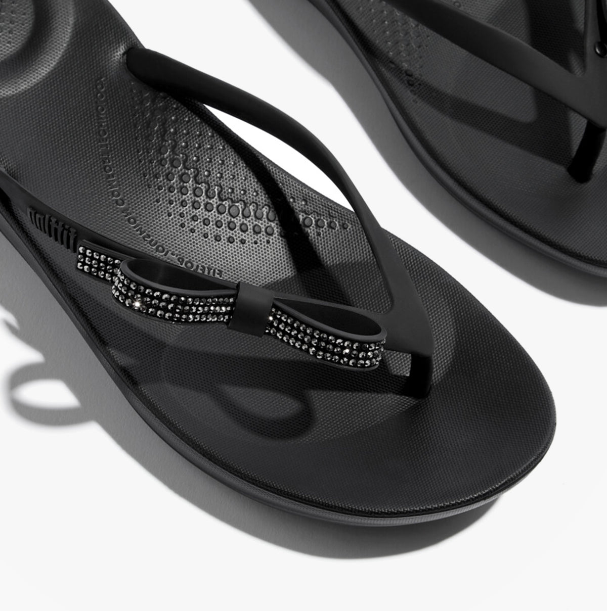 FitFlop iQUSHION GLITZ-BOW Ladies Flip Flops Black top view showcasing bow detail and TPR upper.