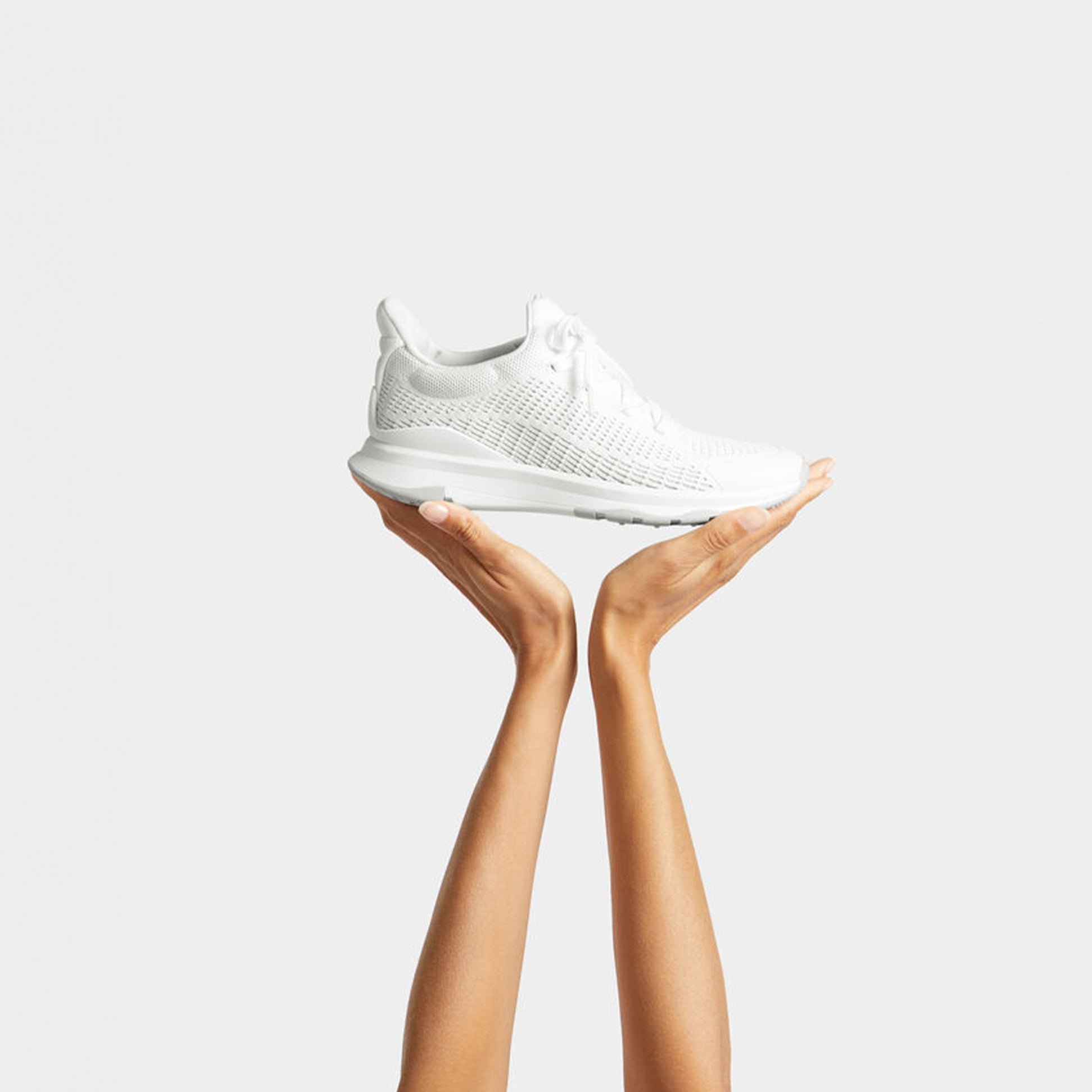 FitFlop VITAMIN FFX KNIT Womens Trainers Urban White Mix held in hands, showcasing a side view with white nylon fabric and rubber sole.