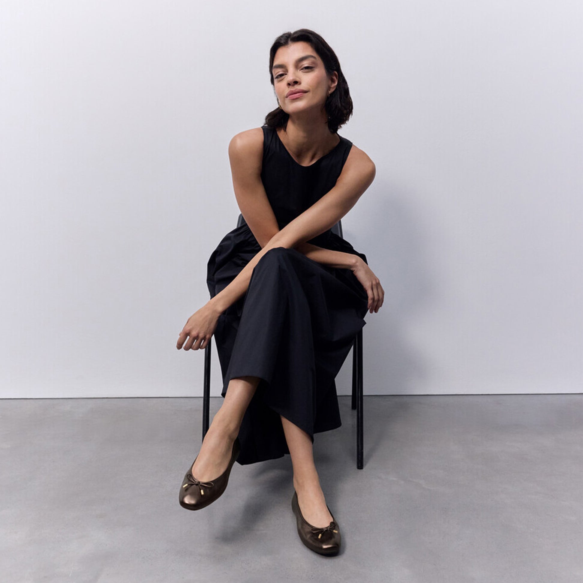 FitFlop DELICATO BOW SOFT METALLIC-LEATHER Ladies Ballet Flats Metallic Chocolate Brown side view worn by model sitting on chair.