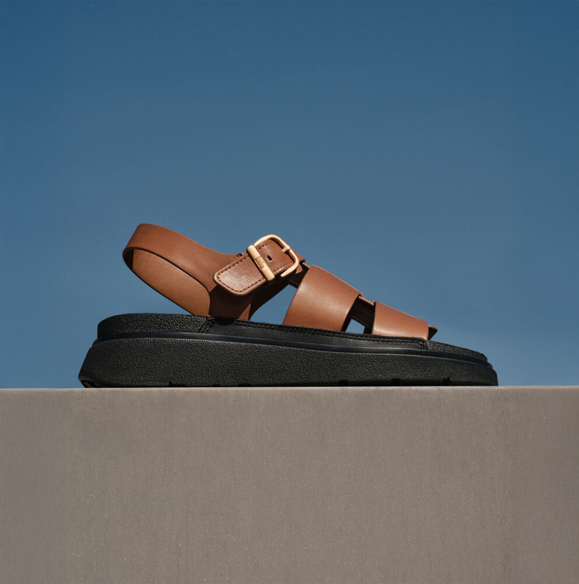 FitFlop GEN-FF LEATHER Womens Fisherman Sandals Deep Tan side view on a gray background with clear blue sky.