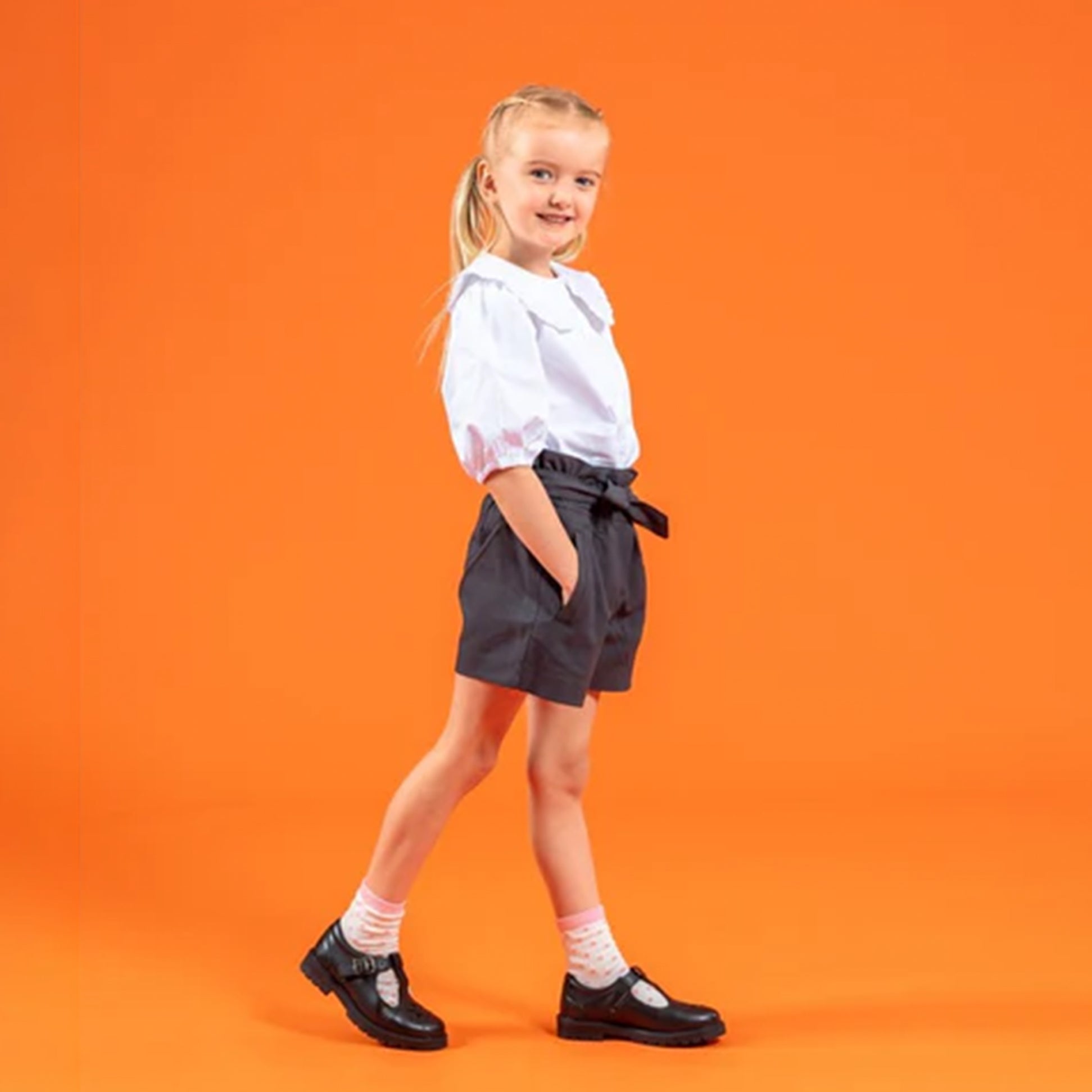 Hush Puppies FIONA Girls Leather School Shoes Black side view worn by a girl on an orange background.