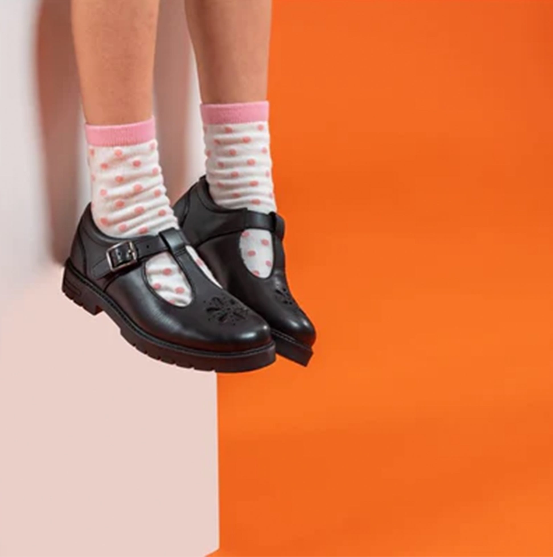 Hush Puppies FIONA Girls Leather School Shoes Black side view with pink socks on a model against an orange background.