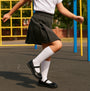 Hush Puppies BETTY PATENT JNR Girls Shoes Black side view, girl playing in the playground wearing school uniform, focus on shoes and skirt.