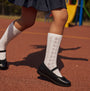 Hush Puppies BETTY JNR Girls Shoes Black side view on child wearing white knee-high socks on playground surface.