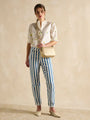 Joules TRENT Womens Cross Body Bag Gold worn by a model in a front view with striped pants and a blouse.